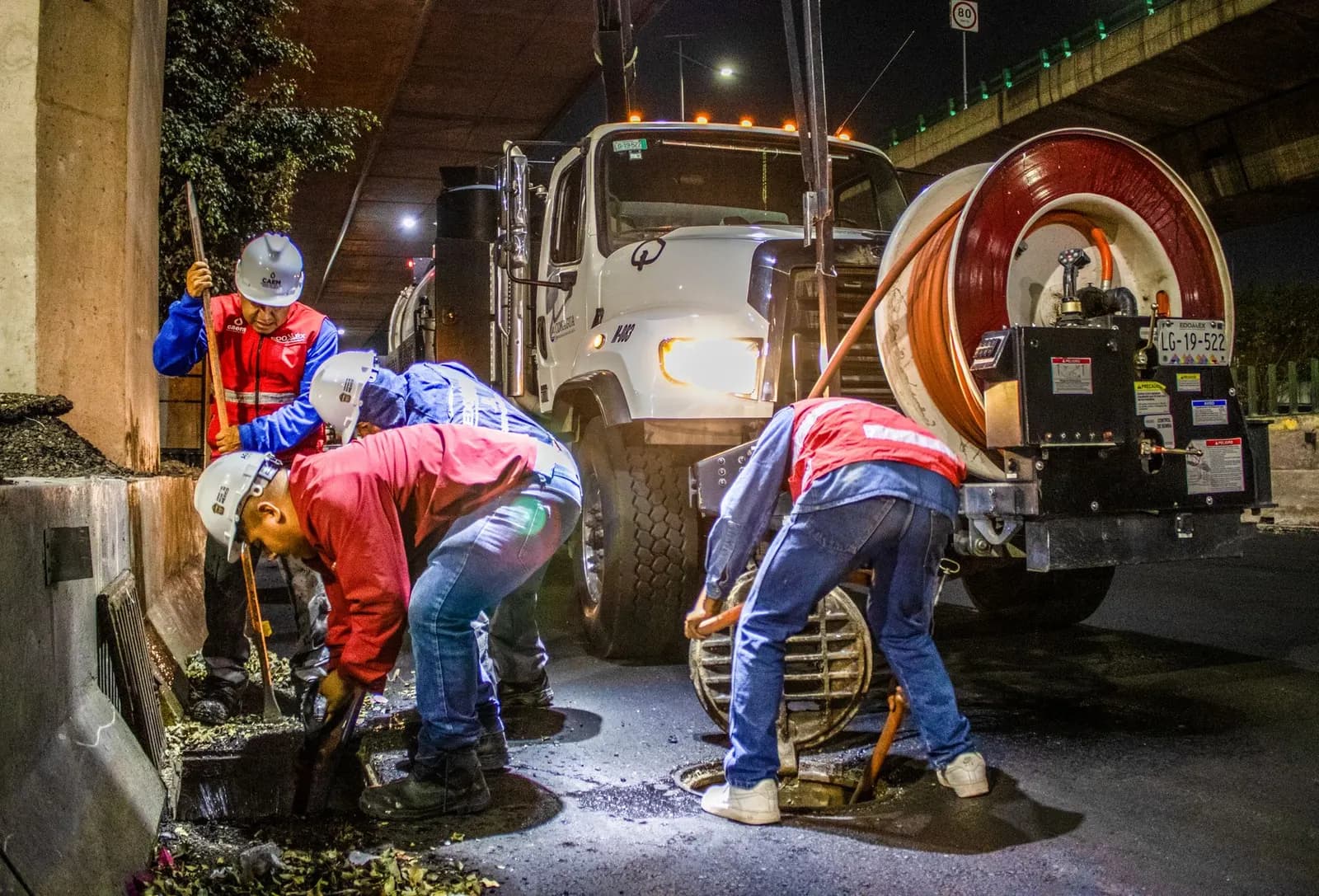 Drainage crew jetting a manhole at night from a tanker